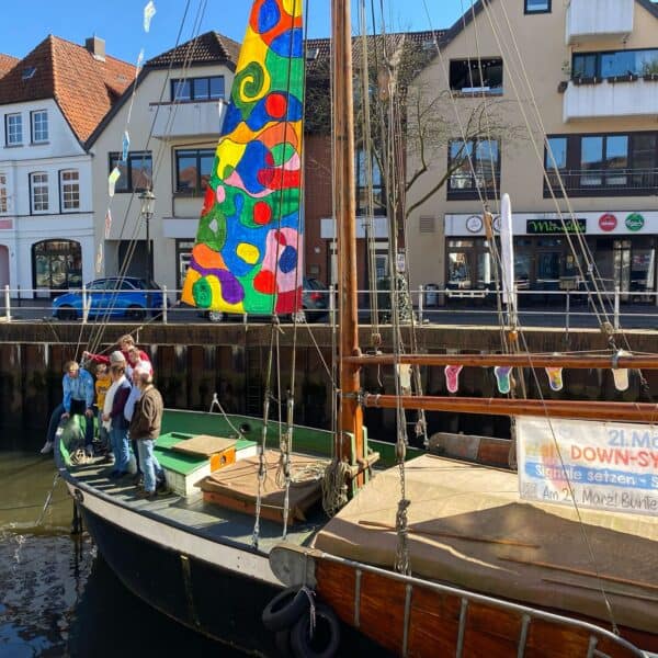 Menschen am Hafen bei Sockentag mit buntem Segel und Boot.