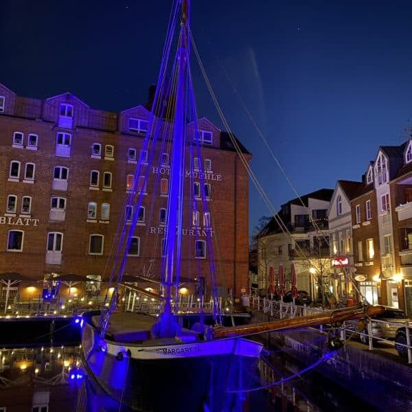 Ein beleuchtetes Segelschiff in einem Hafen bei Nacht, symbolisch für Vielfalt und Inklusion am Welt.