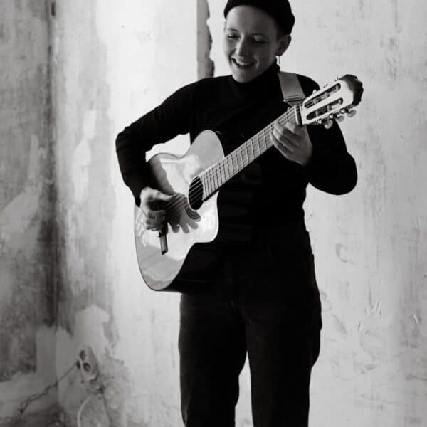 Lia L. Shoshann spielt Gitarre in einem künstlerischen Raum.