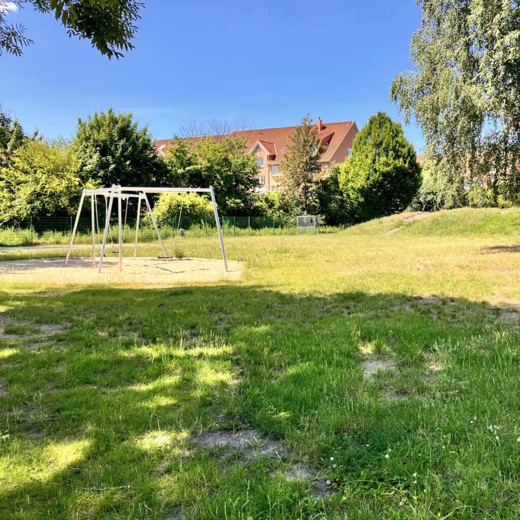 Hier ist eine Abbildung des Spielplatzes Ludwigstraße zu sehen, mit viel Rasenfläche und einer Schaukel.