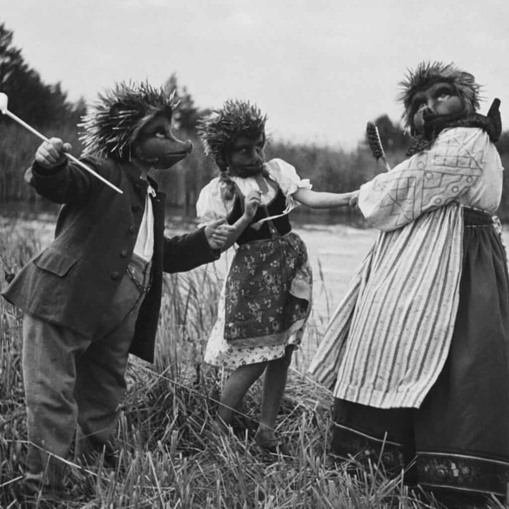Drei als Igel verkleidete Menschen in historischer bäuerlicher Kleidung stehen auf einem Feld